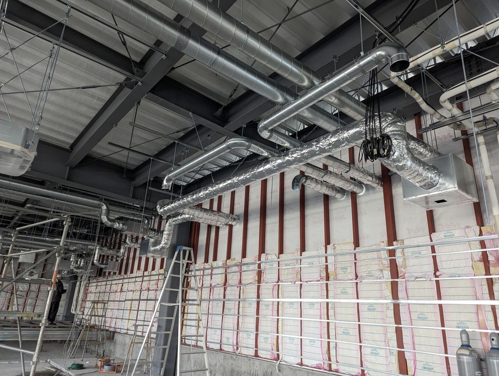 鉄骨の天井内に組んだ空調ダクトと配管、足場が並ぶ現場