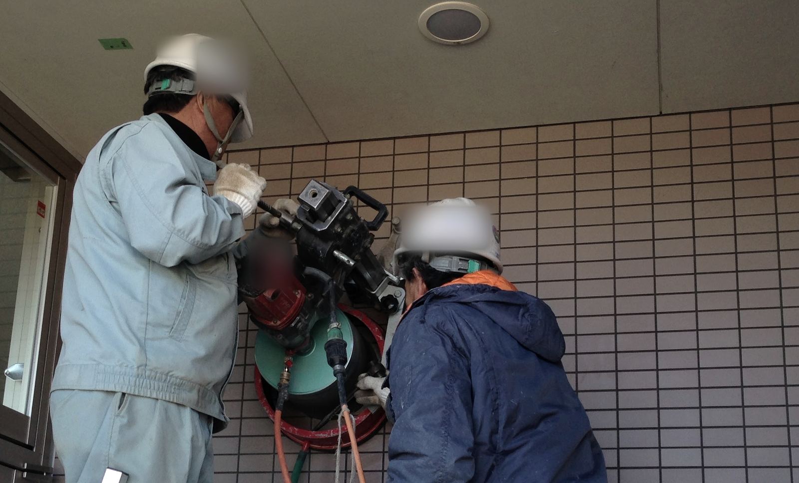 外壁にダクトを通す穴をコアドリルで開ける職人2名