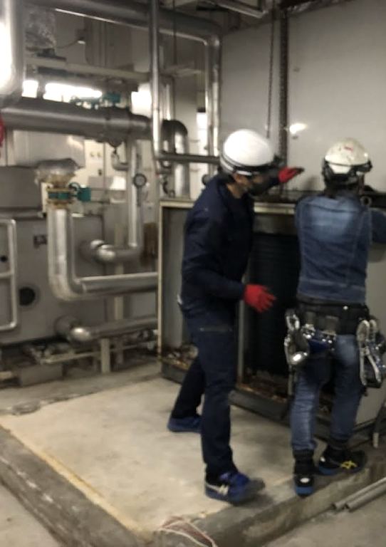 機械室で空調機の作業をするヘルメット姿の職人2名