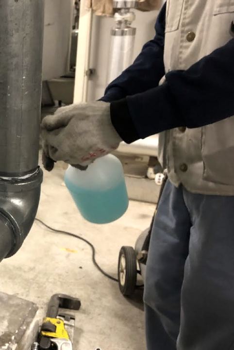 配管の継手に検査液を吹き付けて漏れを確かめる職人の手元